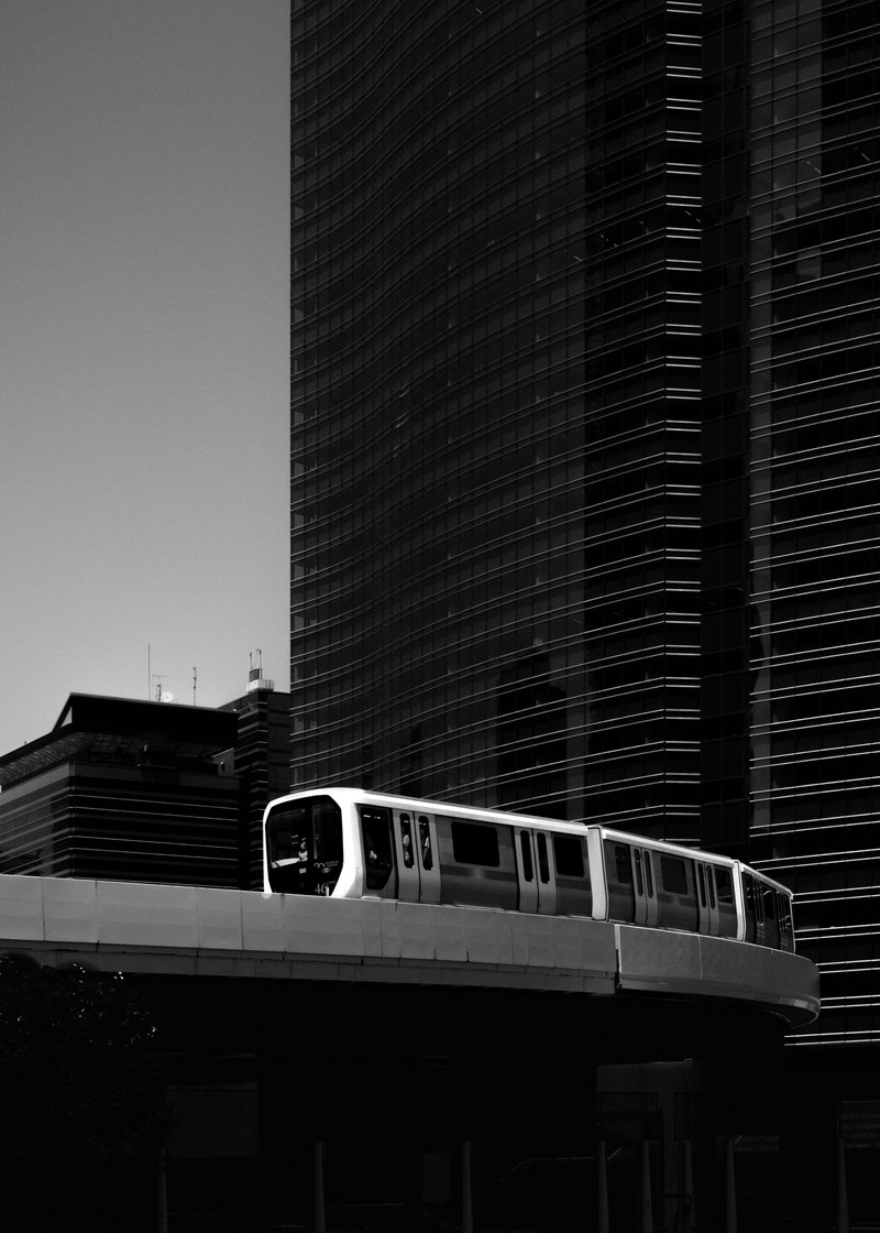 A modern train traveling on an elevated track in front of tall skyscrapers in a city.