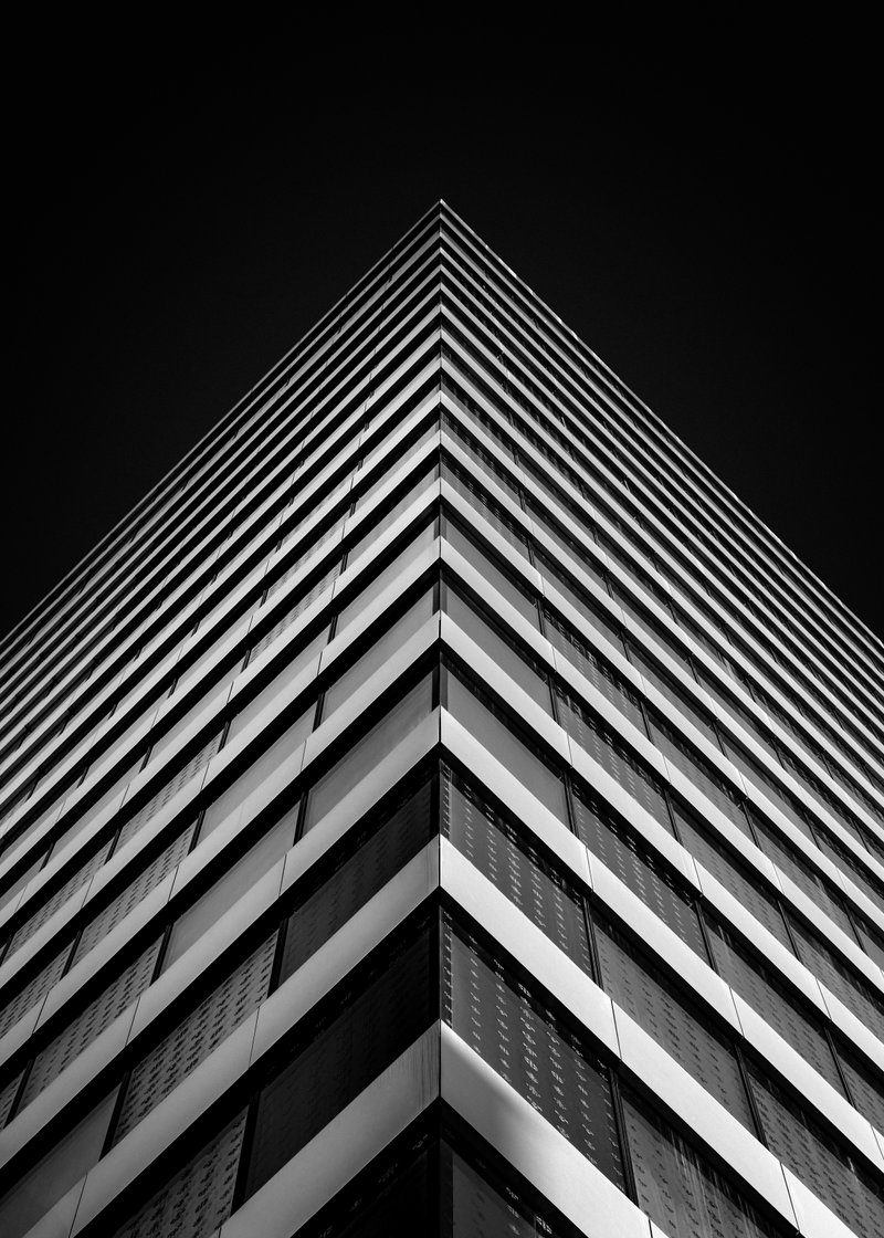 Black and white photo of a modern, multi-story building with horizontal lines and glass windows, taken from a low angle.
