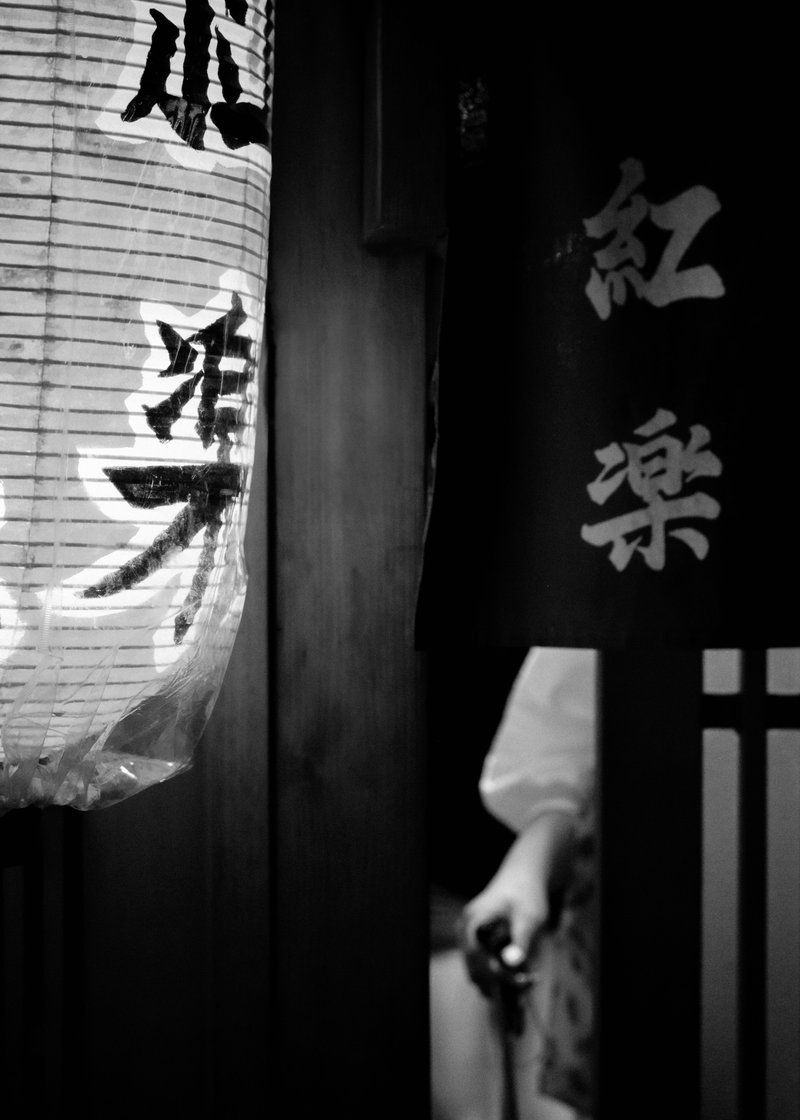 Black and white photo of a Japanese paper lantern and a person holding a paper lantern with Japanese characters, wearing traditional clothing.