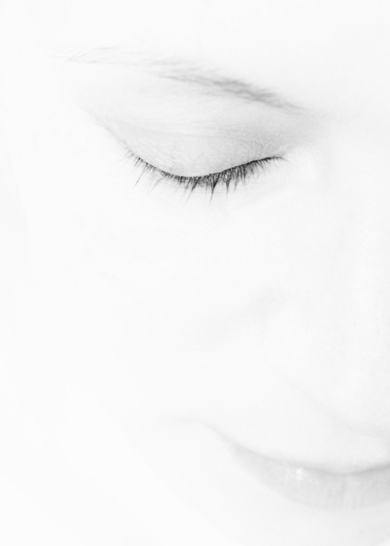 Close-up of a person's face with eyes closed, in black and white, with a soft focus.