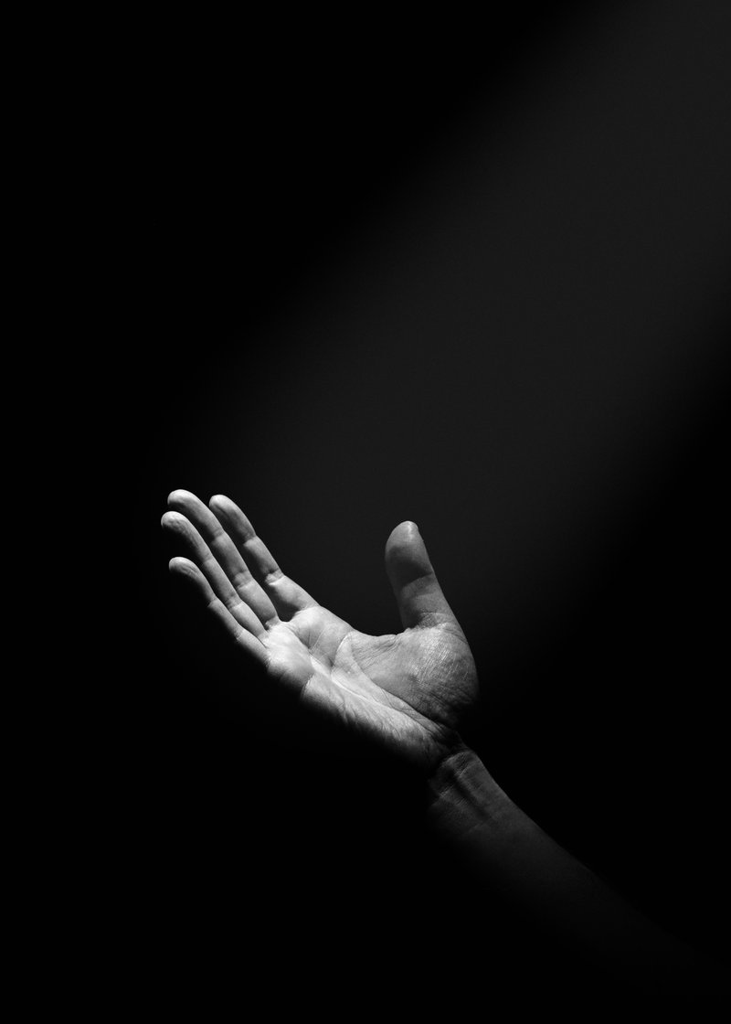 Black and white photo of an open hand with fingers slightly spread, illuminated against a dark background.