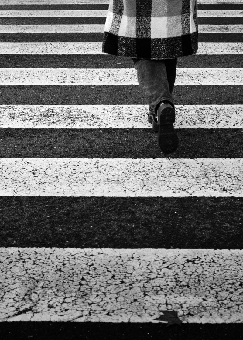 A person walking across a crosswalk, seen from behind, wearing a coat, jeans, and boots.
