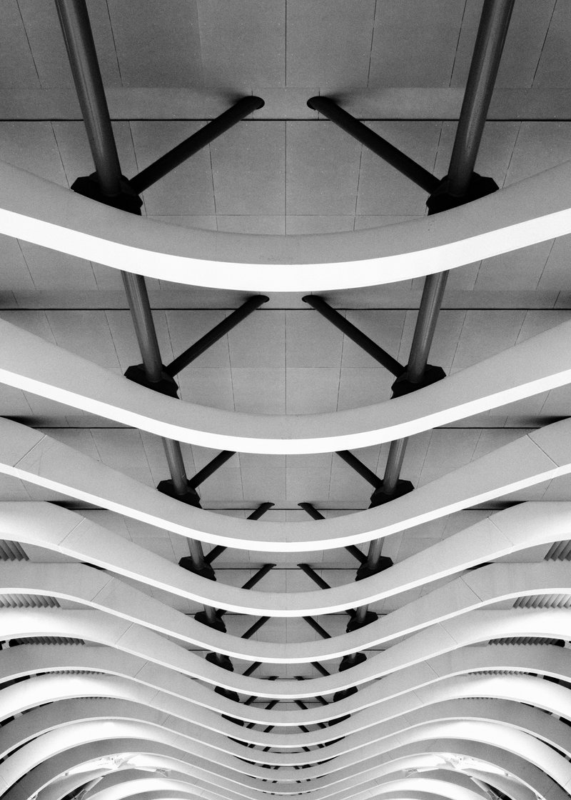 Black and white photo of a modern architectural ceiling with curved white beams and metal supports.