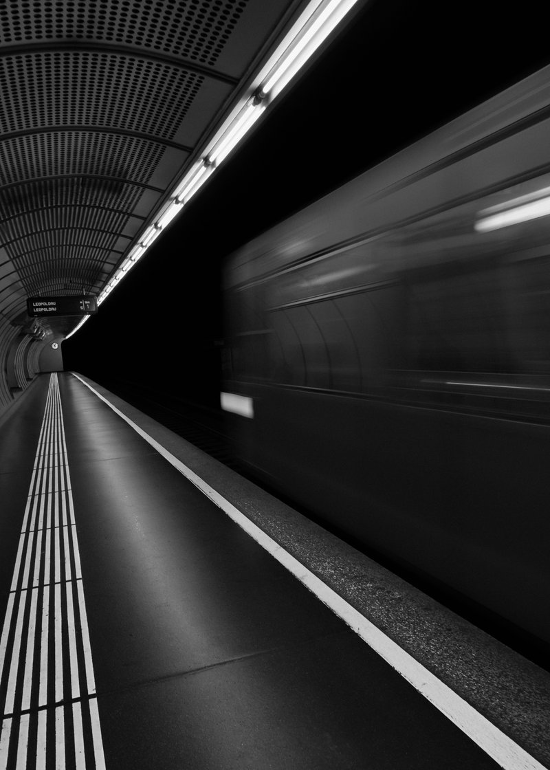 Black and white photo of an underground subway station with a train passing by at high speed.